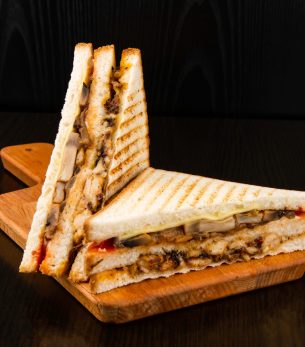 Grilled Chicken Club Sandwich with Mushrooms and Cheese isolated on wooden board side view of fast food on dark background